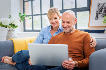 Middle aged couple using laptop together in her modern home