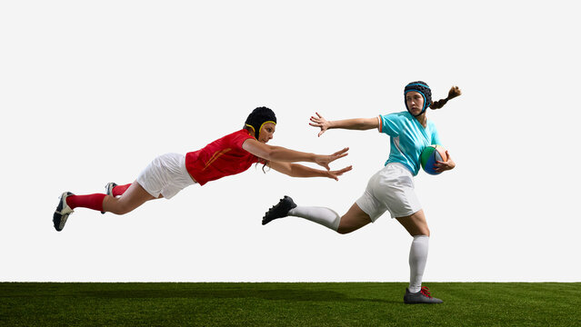 Two female rugby players in action on a green field against white background. Concept of tackle attempt, competition clash, fast pursuit, rugby intensity and field interaction