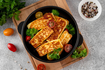 Fried halloumi cheese in a cast iron skillet with parsley and tomatoes on a concrete background. Top view.