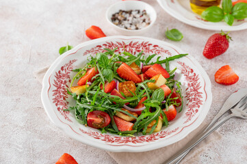 Healthy salad with strawberries, tomatoes, arugula, halloumi cheese and basil on a plate on a...