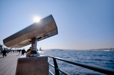 A fixed public telescope positioned along a waterfront promenade, overlooking the scenic ocean...