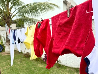 Roupas infantis coloridas a secar no varal num quintal tropical. Uma cena cotidiana, simples e familiar, com uma atmosfera de calor e vida doméstica.