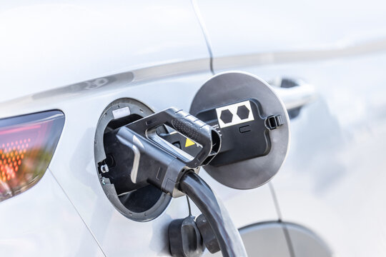 Focus closeup electric vehicle plugged in with EV charger device from blurred background of public charging station powered by renewable clean energy for progressive eco-friendly car concept - Powered by Adobe