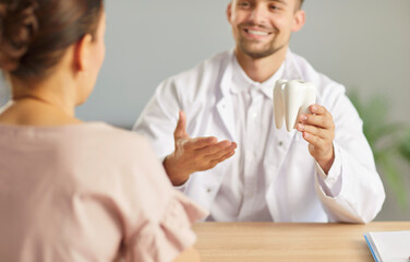 Doctor dentist in a hospital explains dental care to a patient by demonstrating with a tooth model...