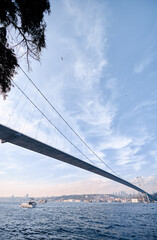 Capturing a stunning suspension bridge spanning over a calm body of water while boats traverse...