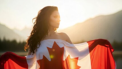 Patriotic young woman wrapped in the Canadian flag. Beautiful girl celebrating Canada Day outdoors in nature with a mountain background at sunset.