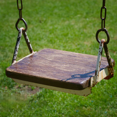 Vintage playground swing in a sunlit yard shows chipped paint and aged wood, evoking memories of...