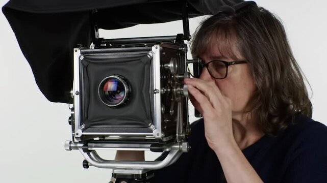 Large format photographer focuses in a studio; plain background