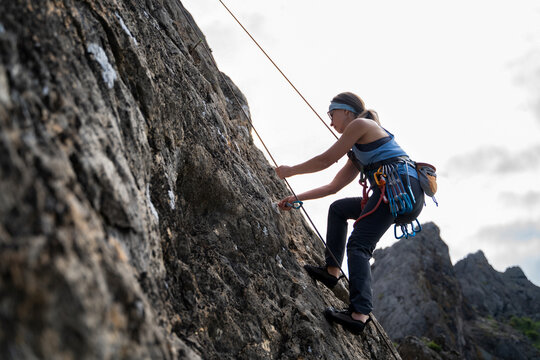 Middle aged female climber removing quickdraw from bolt during top rope descent, outdoor rock climbing gear and safety equipment in use on natural stone wall, outdoor sports activities, full length