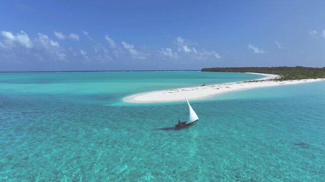 Aerial view of a traditional sailboat gliding through turquoise waters next to a pristine white sandy beach contrasting with lush green vegetation, Bileffahi, Shaviyani Atoll, Maldives.