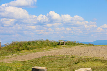 A wooden bench is situated on a high hill, offering a view of the endless blue sky with fluffy...