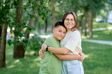 Mother Hugging Son in a Sunny Park with Greenery All Around