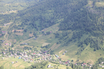 An aerial view of a picturesque mountain village surrounded by dense forests and green fields...