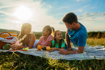 The family is lying on a blanket surrounded by fruit, having a picnic for the last day of summer...