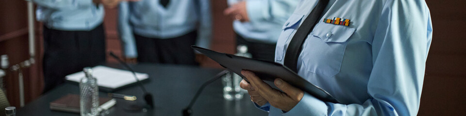 Middle aged Caucasian woman in uniform holding digital tablet standing at conference table with two...