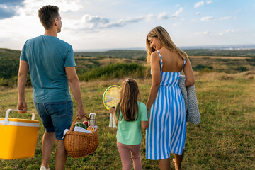 Family on a meadow, mother and daughter holding hands while father carries picnic baskets