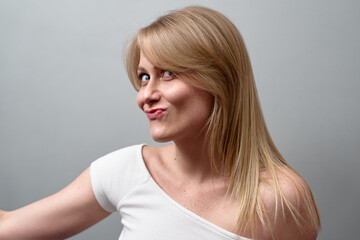 Smiling woman strikes playful pose, expressing personality and confidence. Backdrop is plain...