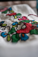 Close-up of colorful hand embroidery featuring vibrant flowers on white fabric, showcasing...