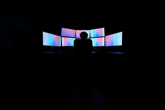Person using multiple computer screens for gaming coding or data analysis setup dark