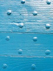 A textured blue wooden surface is displayed, featuring numerous small bumps and gleaming water droplets
