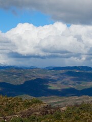 A vast mountain landscape unfolds with green hills, shadowy valleys, and distant peaks.
