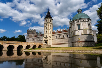 Krasiczyn Castle in Podkarpackie, Poland – Renaissance fortress with dome, towers, stone bridge and moat, beautifully reflected under blue sky and clouds