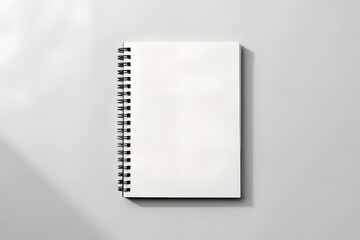 Blank white spiral notebook on a gray surface with shadow and black spiral binding detail