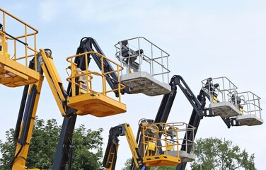 Group of black and yellow aerial platforms of cherry pickers against cloudy sky 