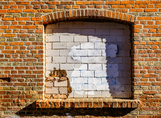 Brick wall with a bricked-up window and remnants of old plaster showing patchy texture and shadows...