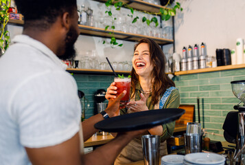 Female barista working in a coffee shop at the counter and gives a refreshing drinks to a male waiter to serve to the customer.