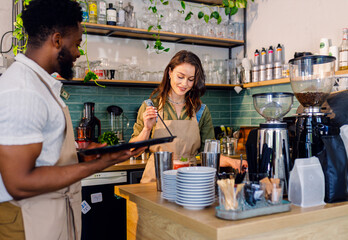 Female barista working in a coffee shop at the counter and gives a refreshing drinks to a male...
