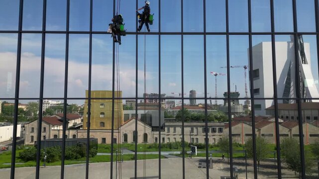 Europe, Italy, Milan  07,22,2025 Two skyscraper window cleaners work suspended in the air - drone aerial view of acrobatic window cleaners  near the Prada Foundation new skyline of the fashion city 