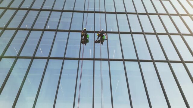 Europe, Italy, Milan  07,22,2025 Two skyscraper window cleaners work suspended in the air - drone aerial view of acrobatic window cleaners  near the Prada Foundation new skyline of the fashion city 