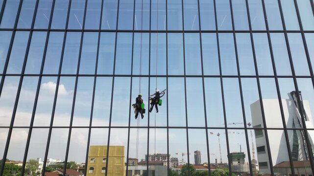 Europe, Italy, Milan  07,22,2025 Two skyscraper window cleaners work suspended in the air - drone aerial view of acrobatic window cleaners  near the Prada Foundation new skyline of the fashion city 