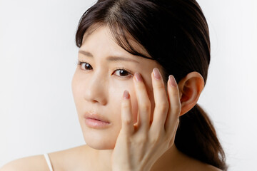 目元の悩みを気にする若い女性（白背景）
