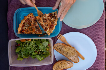 Stockholm, Sweden Hands serve a piece of homemade quiche onto plastic plates and a salad.