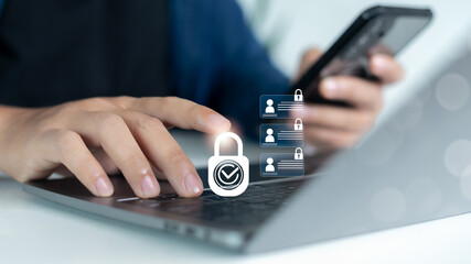 Close-up of a hand using a laptop and smartphone with lock icon overlay, representing...