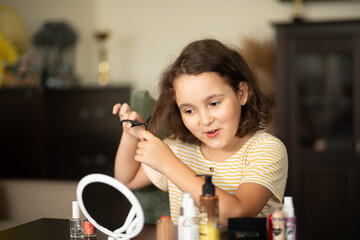 Cute little girl cutting her hair with scissors at home
