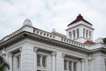 Obraz premium Architectural detail of a historic white Dutch colonial building in Kota Tua, Jakarta, featuring a tower, windows, and classic cornices under a cloudy sky.