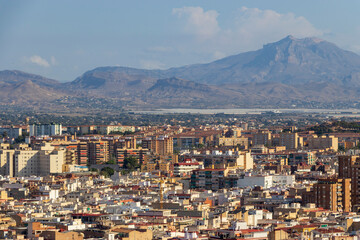 Panoramic view of Alicante, showcasing modern buildings amidst stunning mountains in the background. A vibrant urban landscape displays the city's architectural diversity.