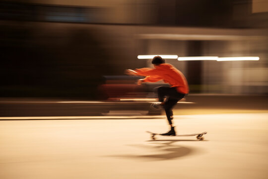 Side view of male skater balancing on one leg while riding longboard on city street at night.