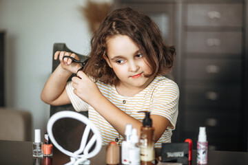 Cute little girl cutting her hair with scissors at home