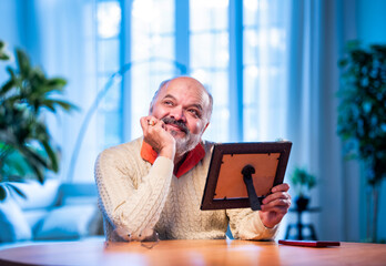 Elderly Indian man holding framed photo with love, lost in memory and emotion