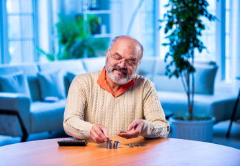 Old Indian man with coin stack and calculator managing money at home table