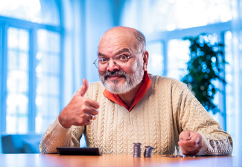 Old Indian man with coin stack and calculator managing money at home table