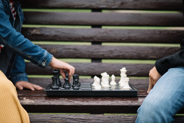 Kids girl and teenager boy playing chess outdoor in a summer park sitting on bench