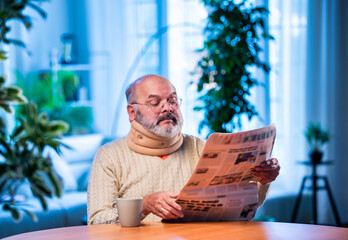 Senior Indian man with newspaper and tea at table during quiet morning routine at home