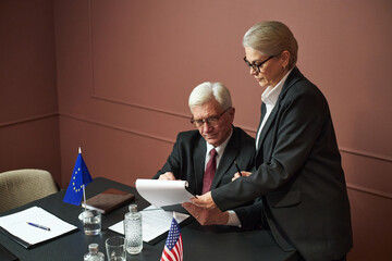 Middle aged Caucasian woman and senior Caucasian man discussing documents at table with United...