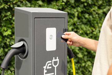 Man holds payment card near EV charging station terminal. Showcases contactless payment, fast, convenient tech, modern energy solutions, smart charging, and eco-friendly transport services.