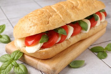 Tasty sandwich with mozzarella cheese, tomatoes and basil on light tiled table, closeup
